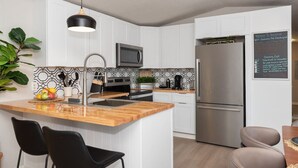 A modern kitchen with white cabinets, a wooden island, black bar stools, a stainless steel refrigerator, and a chalkboard menu. - Dragonfly Beach Retreat (Grayland)