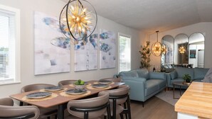 A modern dining area with a wooden table, beige chairs, and abstract wall art. - Dragonfly Beach Retreat (Grayland)