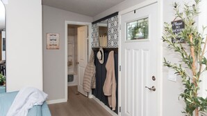 A hallway with a blue sofa, a coat rack with coats, a door with a 'No Smoking' sign, and a plant. - Dragonfly Beach Retreat (Grayland)