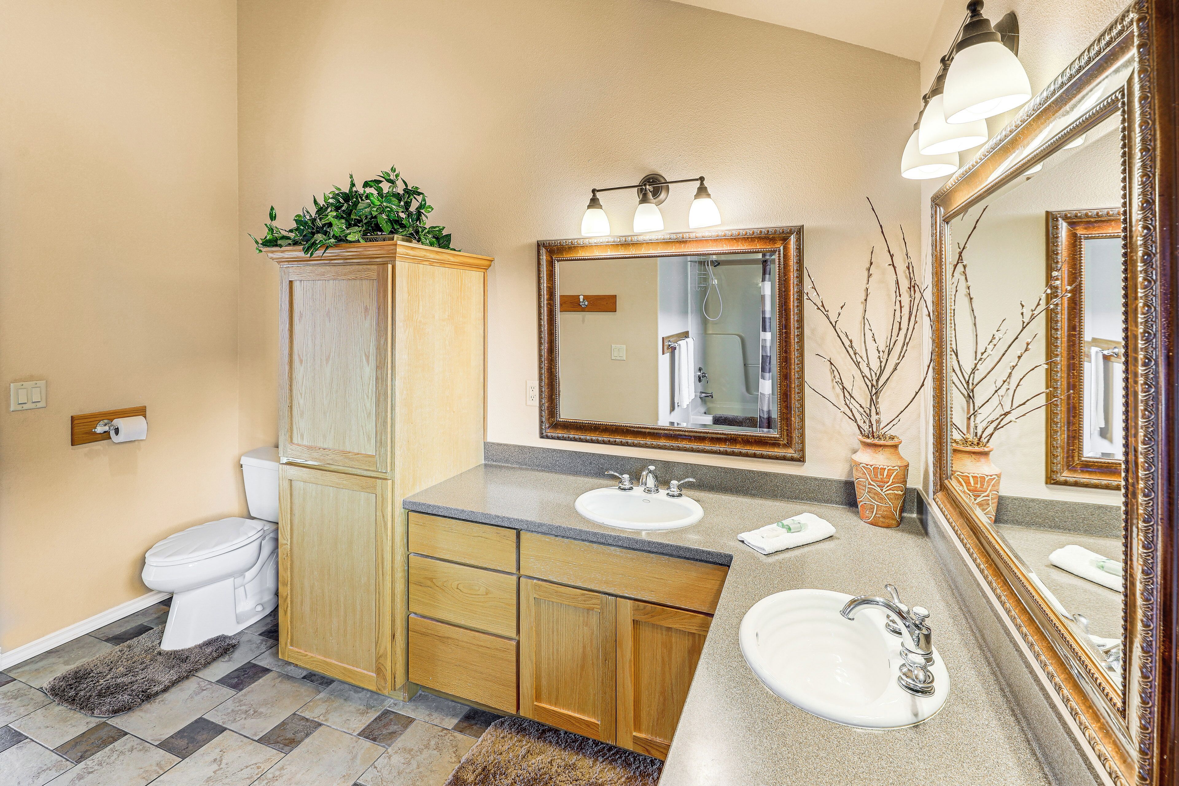 A bathroom with a toilet, wooden cabinet, two sinks, and a large mirror.