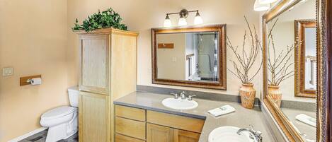 A bathroom with a toilet, wooden cabinet, two sinks, and a large mirror.