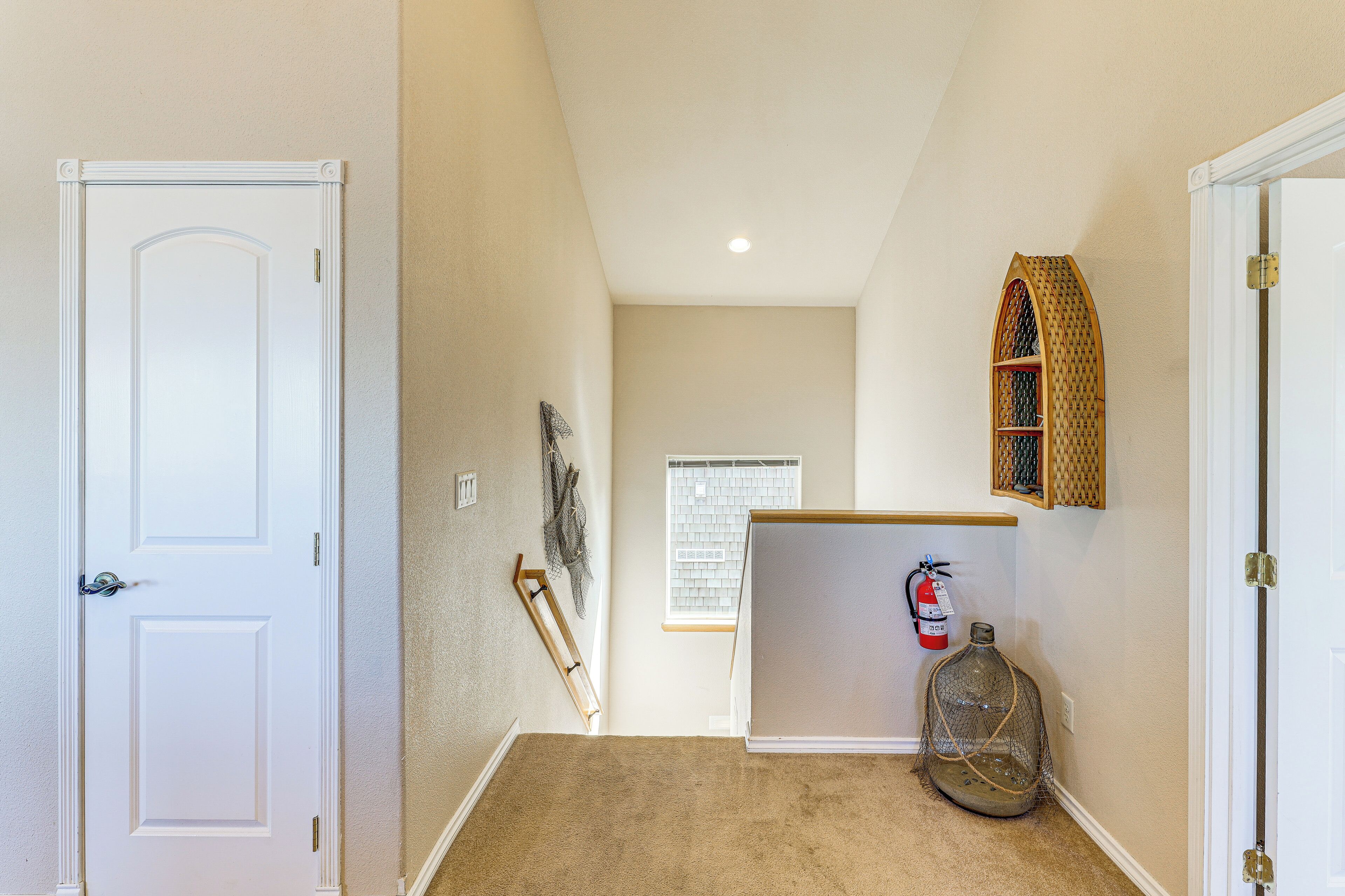 A hallway with a white door, a fire extinguisher, and a window.