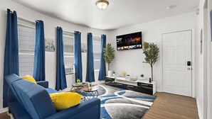 Una sala de estar moderna con un sofá azul, una mesa de centro y un televisor montado en la pared.