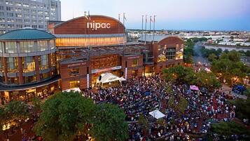 Un gran centro de convenciones con un cartel destacado que dice 'nipac', varios niveles y una multitud reunida en el exterior.