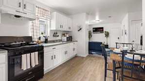 Una cocina moderna con armarios blancos, una estufa negra y una zona de comedor con mesa y sillas de madera.