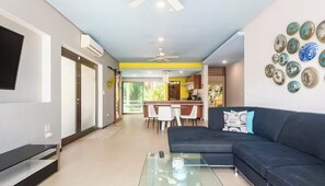 A modern living room with a sofa, a glass coffee table, and a kitchen in the background.
