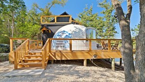 Une cabane dans les arbres avec un escalier en bois menant à une plateforme dotée d’un espace salon.