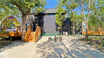 A building with a wooden staircase leading to a covered area, surrounded by trees and gravel.