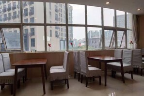 A dining area with tables and chairs, large windows, and a view of buildings. - Homeinn Pebble Hotel (Shanghai Cao'an Textile Market Dingbian Road Subway Station) (Shanghai)
