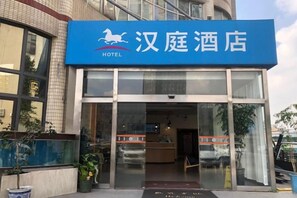 Ein Hotel Eingang mit einem blauen Schild, Glastüren und einem sichtbaren Empfangsbereich.