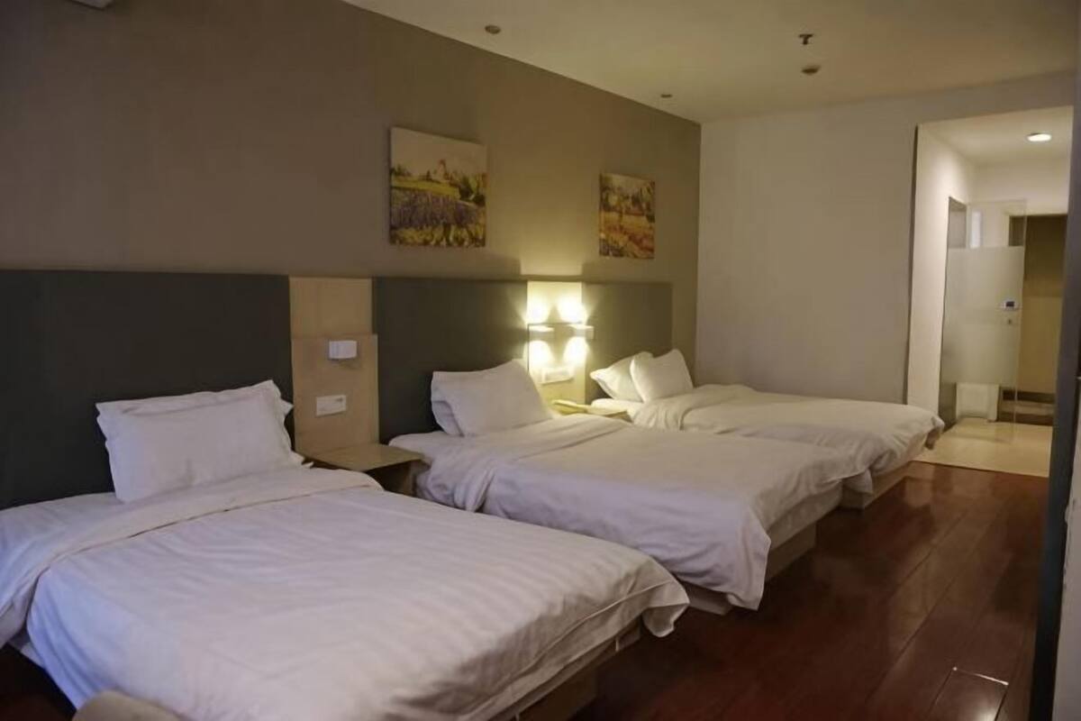 A hotel room with three beds, a headboard, wall-mounted lamps, and a door leading to a bathroom.