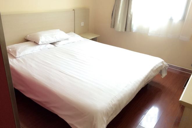 A bed with white linens, a nightstand, and a window with curtains.