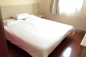 Ein Bett mit weißer Bettwäsche, ein Nachttisch und ein Fenster mit Vorhängen.