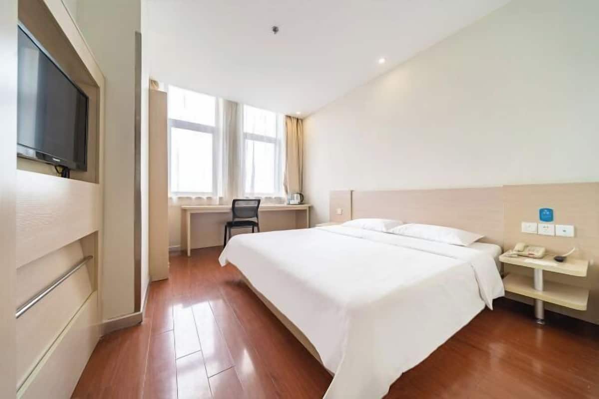 A hotel room with a bed, a desk, a chair, a TV, and a window.