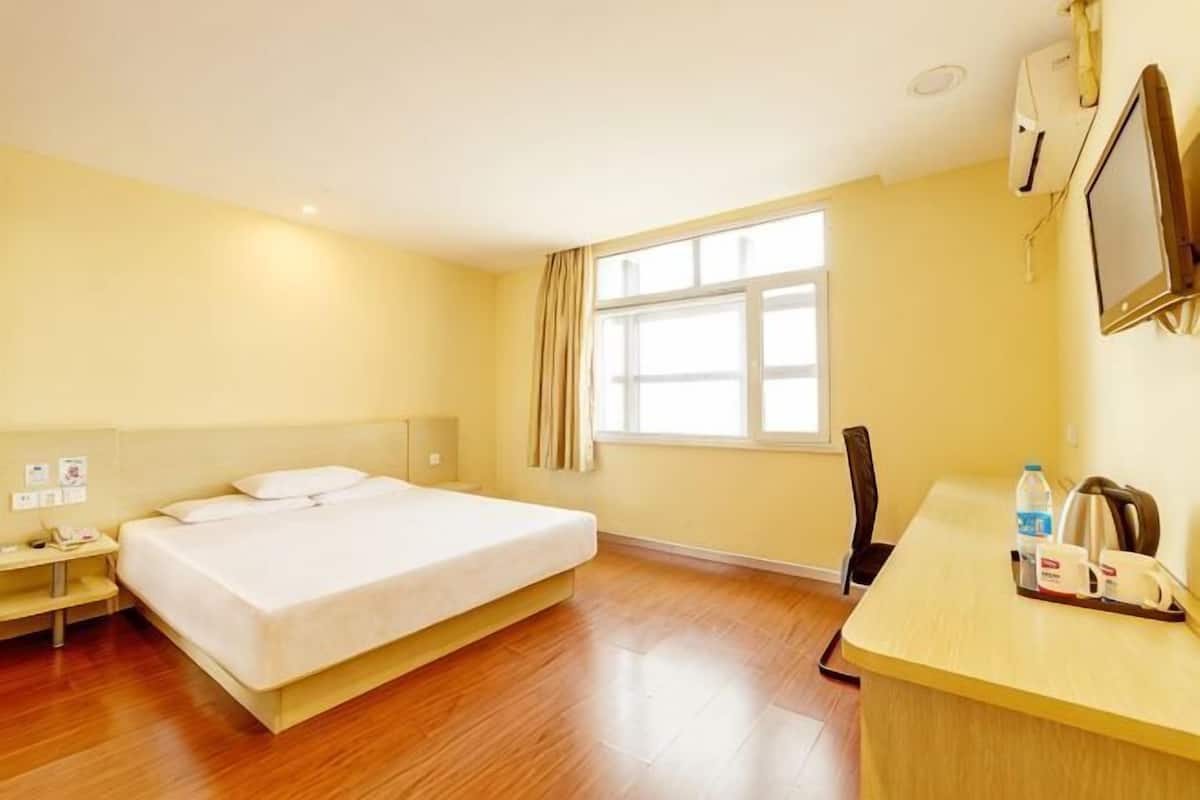 A hotel room with a bed, desk, chair, and a window with curtains.