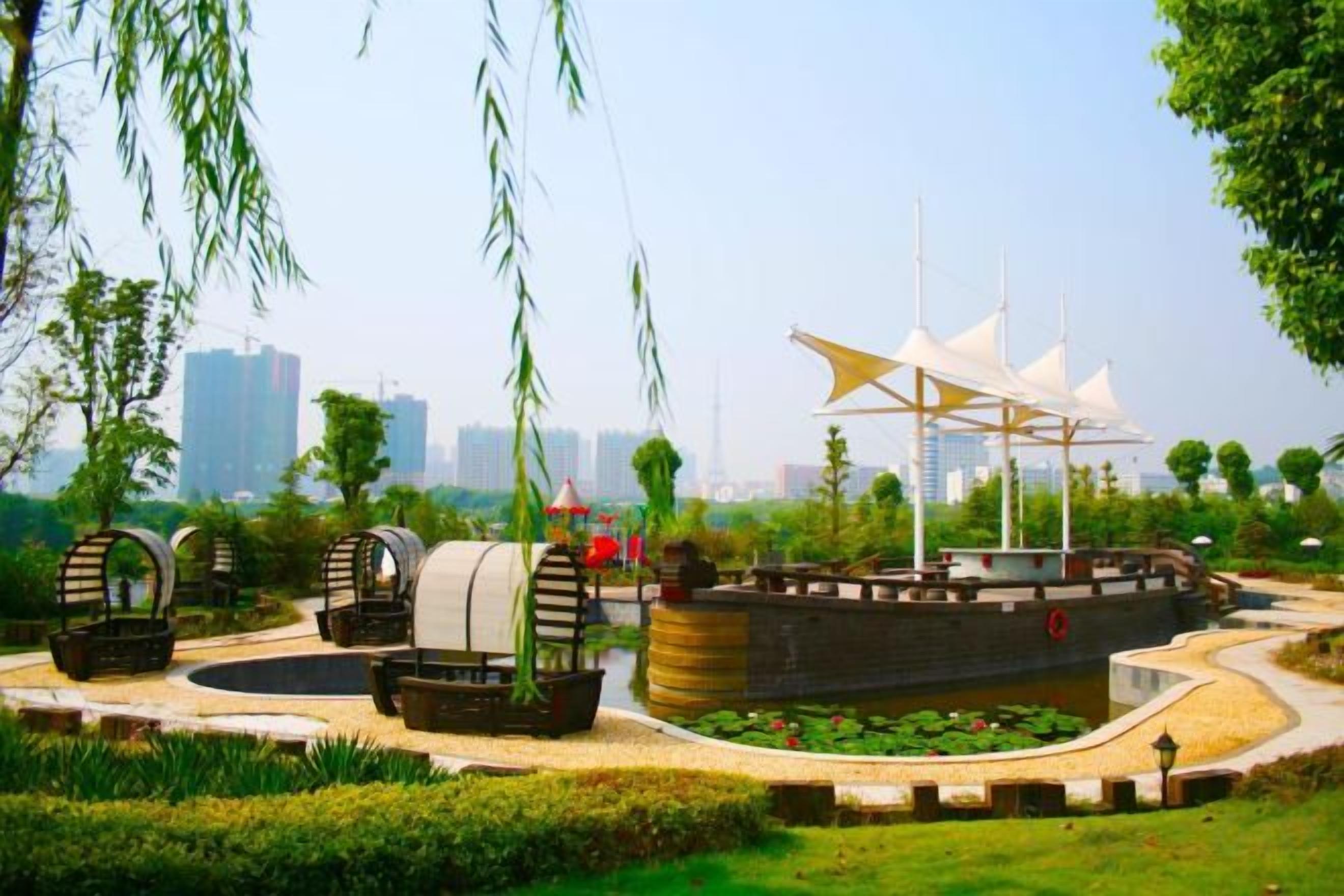 A park with a large ship-shaped structure, a circular water feature, and a pathway.