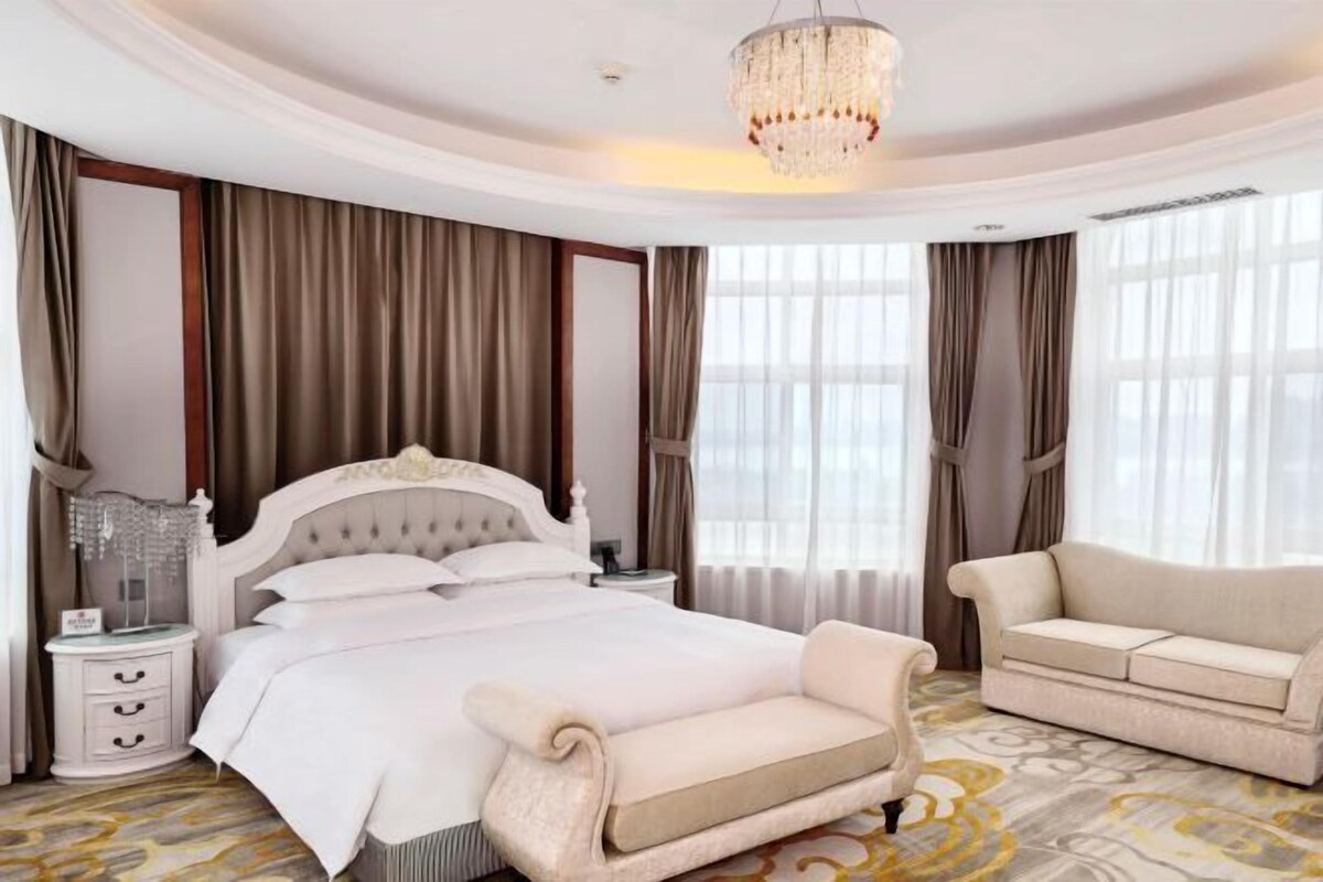 Une chambre à coucher avec un grand lit, un canapé, une table de chevet et un lustre.