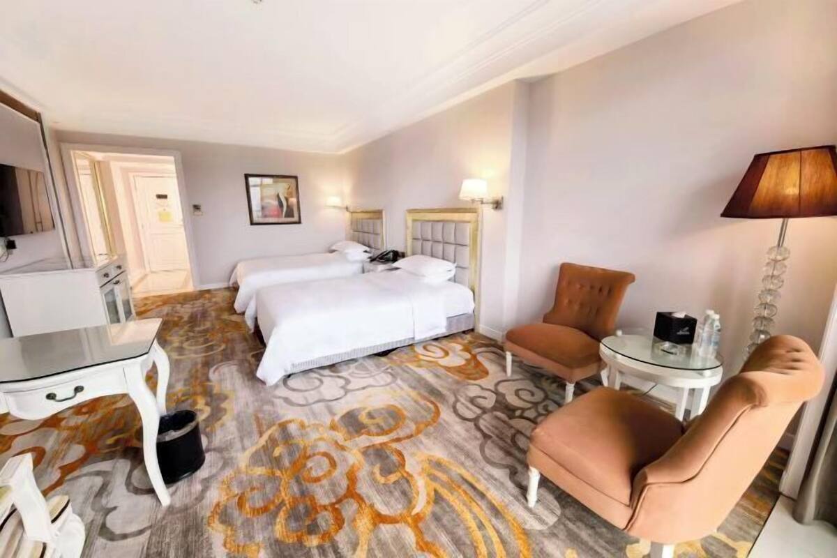 A hotel room with two beds, a desk, a chair, a lamp, and a carpeted floor.