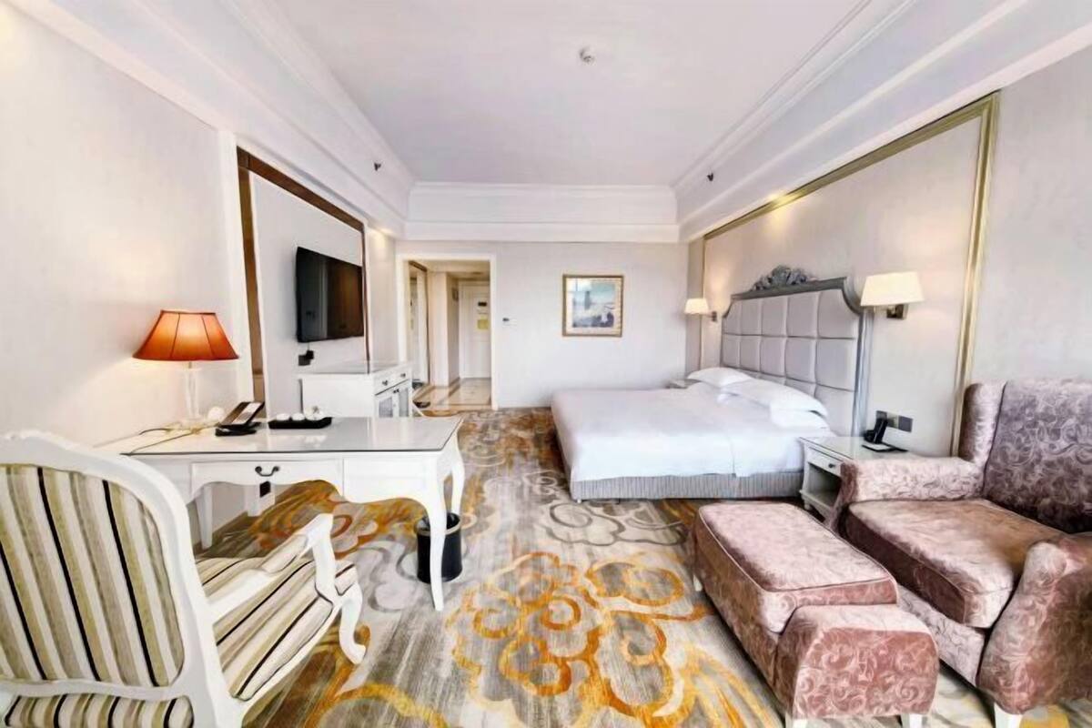 Et hotelværelse med seng, skrivebord, stol, sofa og fjernsyn.
