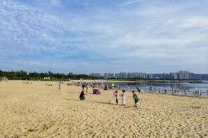 Una playa arenosa con gente, una masa de agua y un horizonte urbano a lo lejos.
