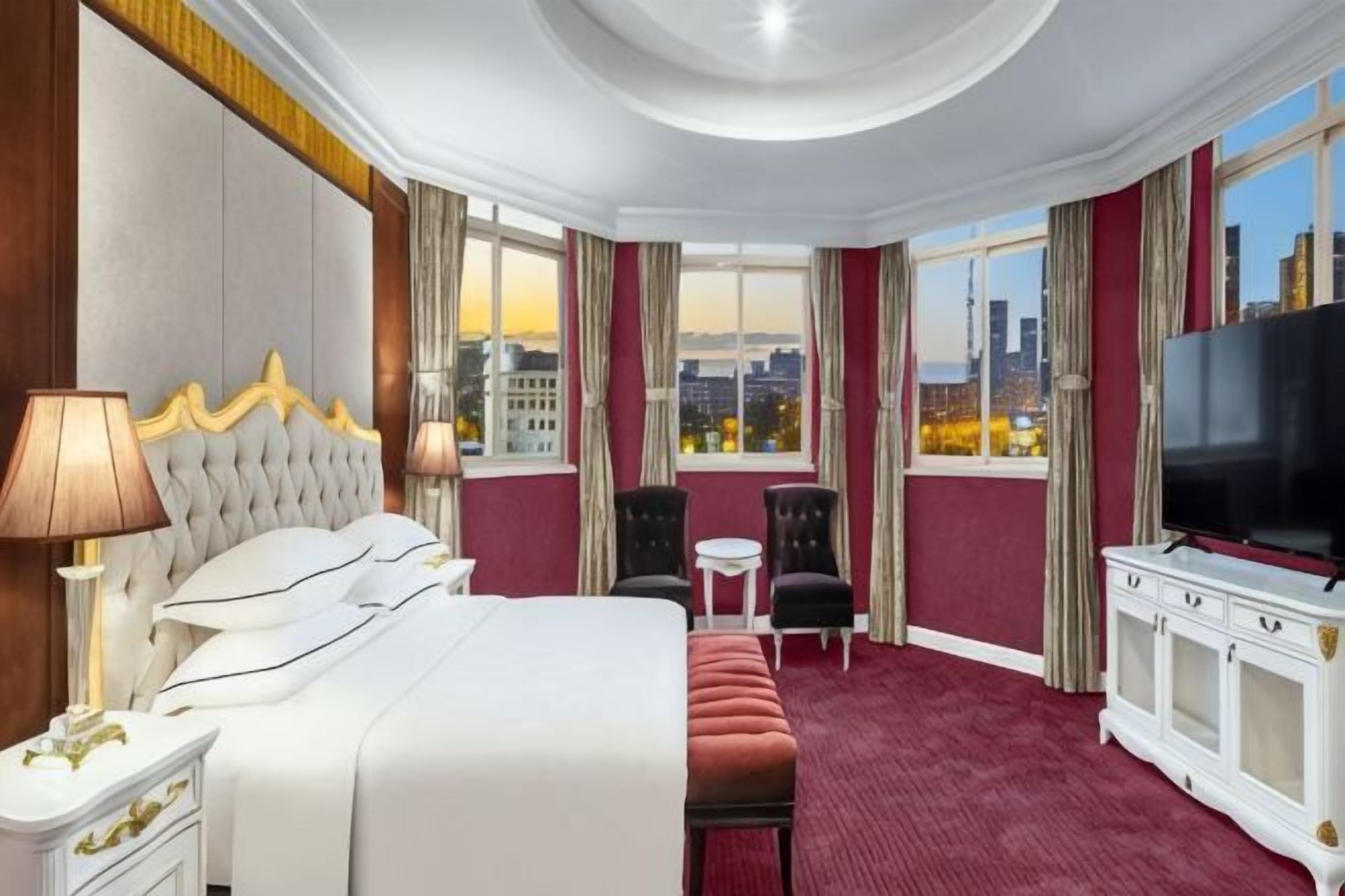 A hotel room with a large bed, a TV, a desk, and a view of the cityscape.