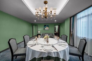 Un salón de conferencias con una mesa redonda dispuesta para una reunión, equipado con sillas, un candelabro y un ventanal que proporciona luz natural.