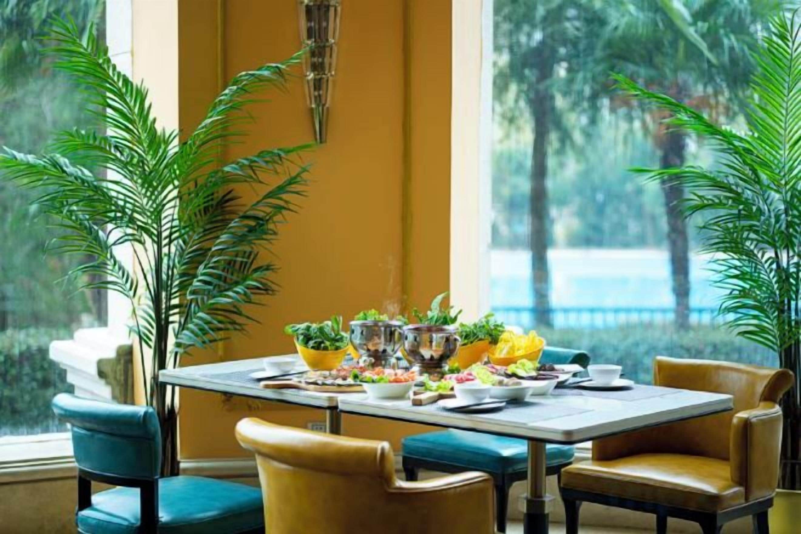 Comedor con una mesa dispuesta para cuatro personas, rodeada de sillas y grandes ventanales con vistas a zonas verdes.