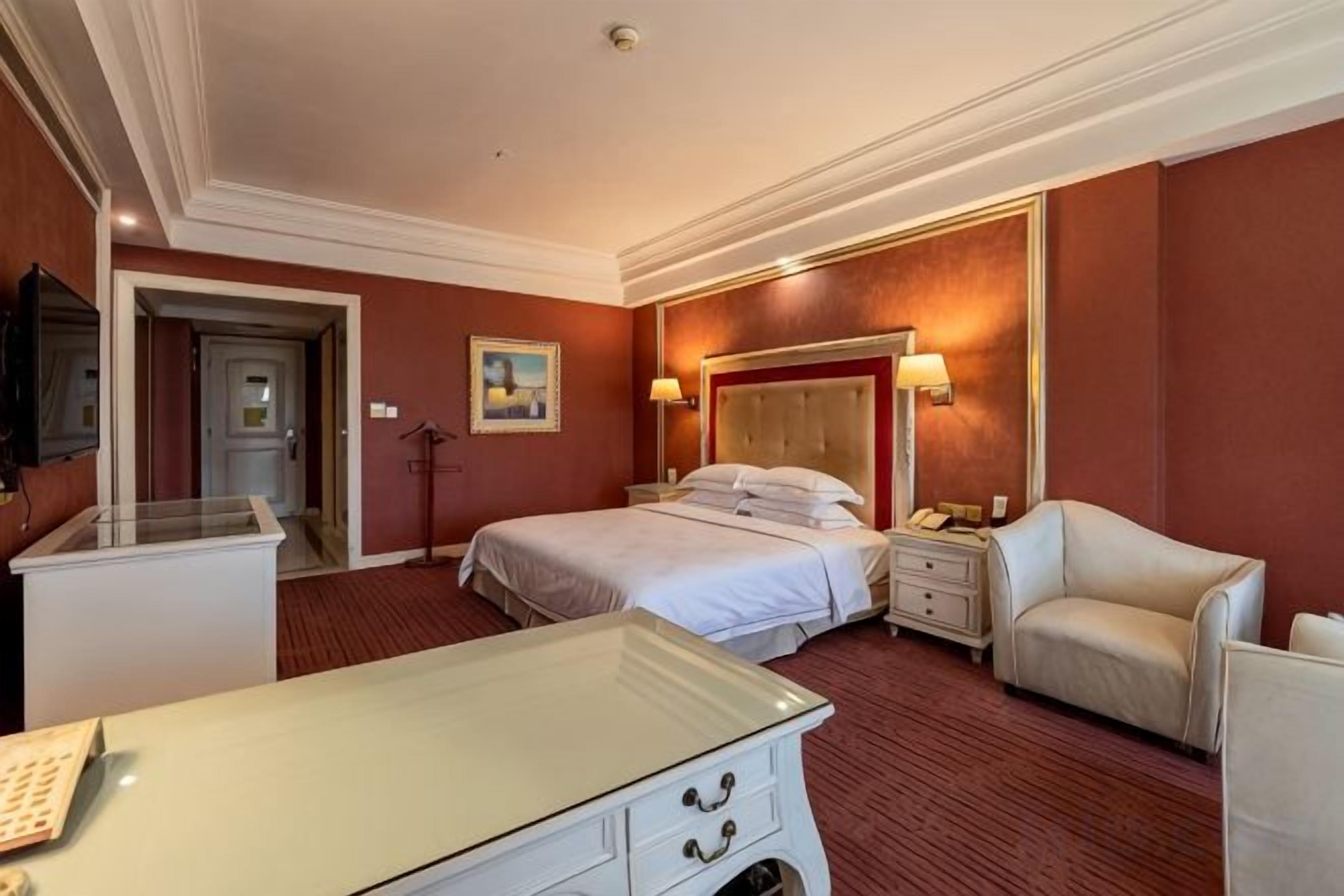 Una habitación de hotel con una cama, mesitas de noche, un escritorio, una silla y un televisor.