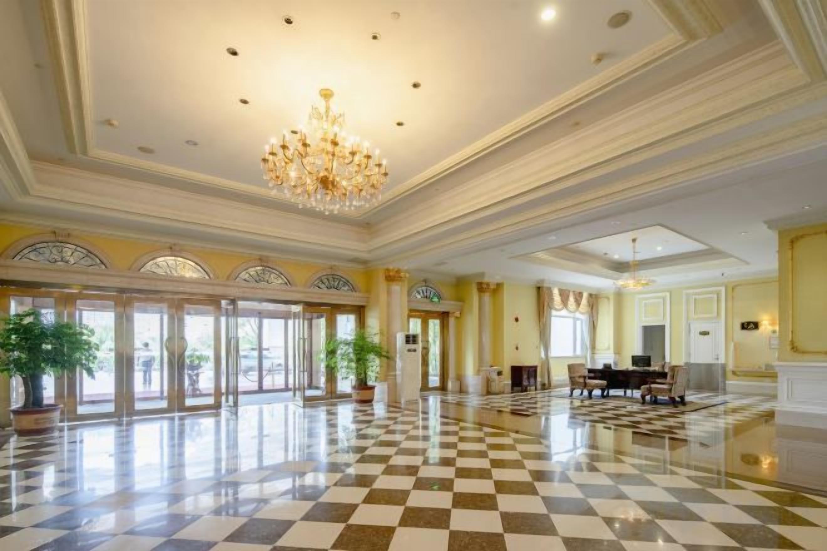 A spacious lobby with a checkered floor, a chandelier, and a piano.