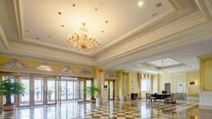Un'ampia hall con pavimento a scacchi, grandi finestre e un lampadario.