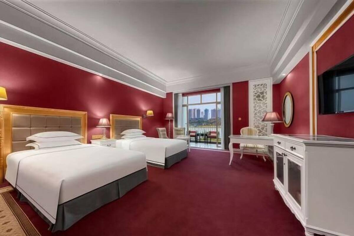 Et hotelværelse med to senge, et skrivebord, en stol og et stort vindue.