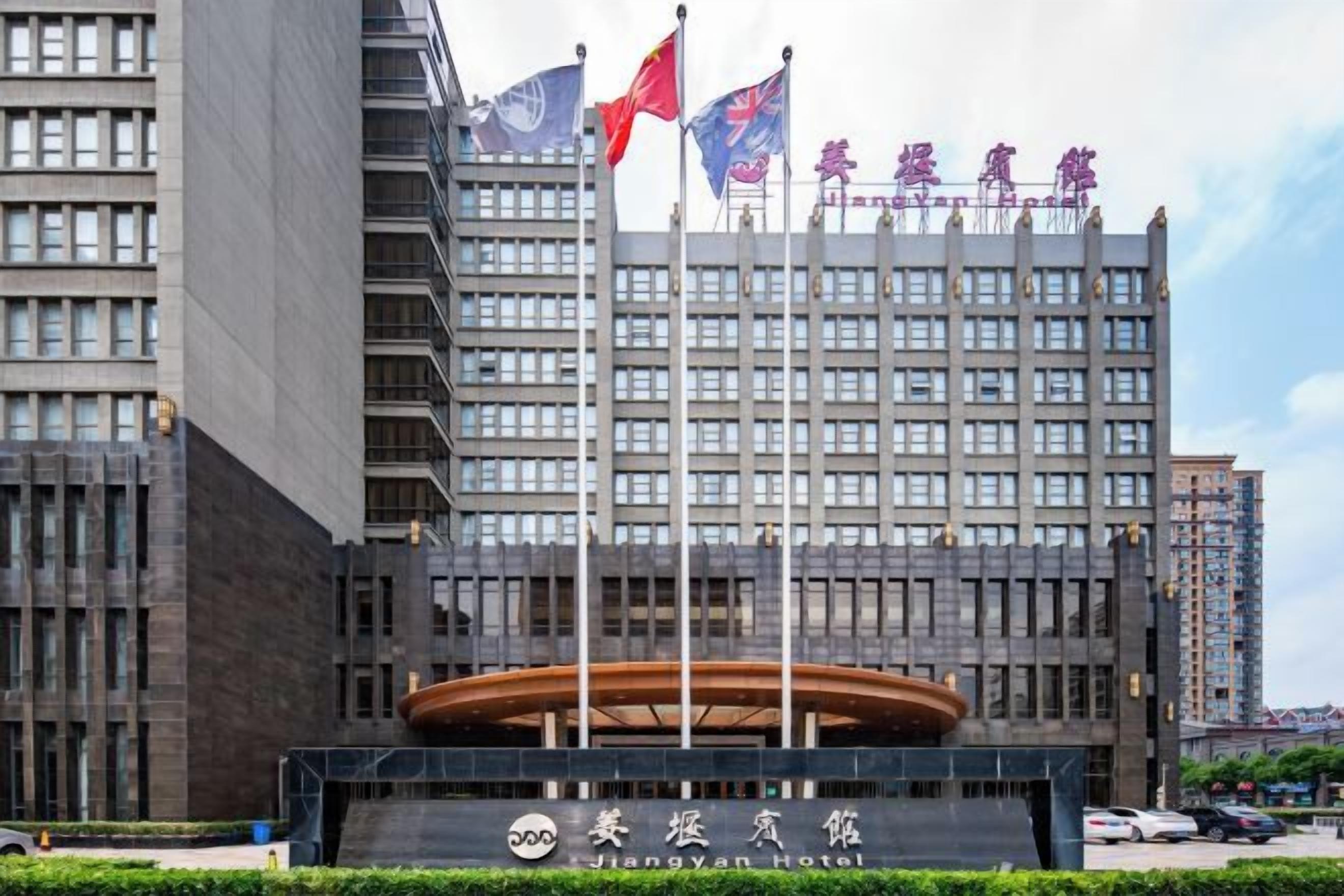 A modern building with a large entrance, multiple flags, and a sign indicating it is the Jiangyan Hotel.