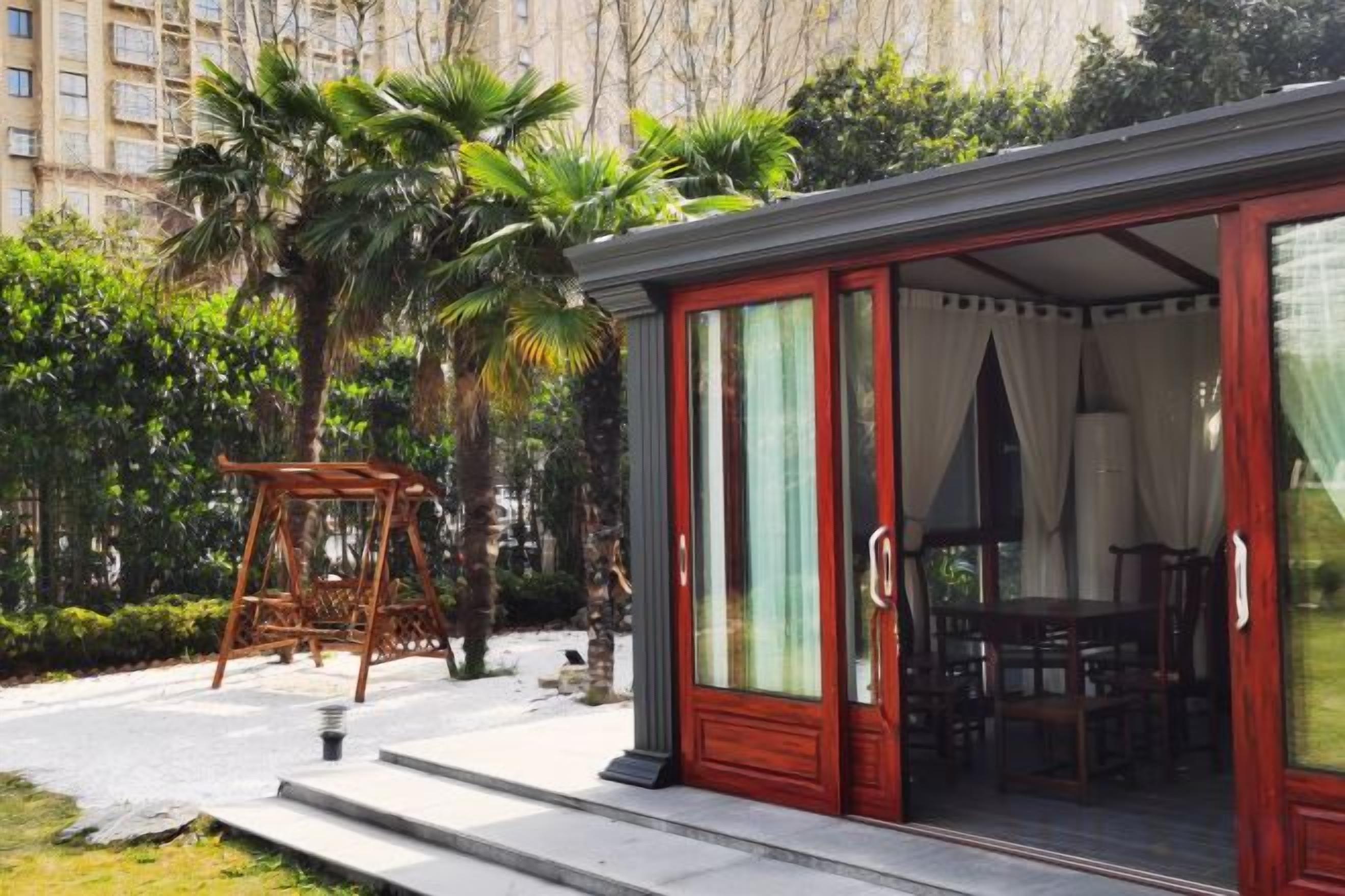 A covered outdoor seating area with a table and chairs, a swing set, and a red door leading to an interior space.