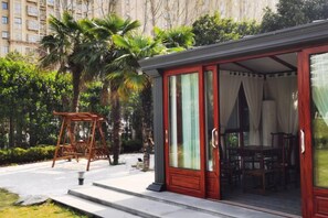 A covered outdoor seating area with a table and chairs, a swing set, and a red door leading to an interior space. - Jiangyan Hotel (Taizhou)
