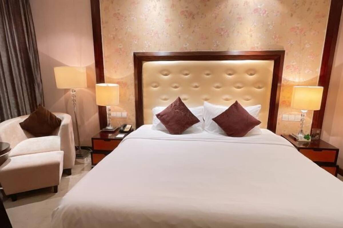 A hotel room with a large bed, two nightstands, a chair, and a lamp.
