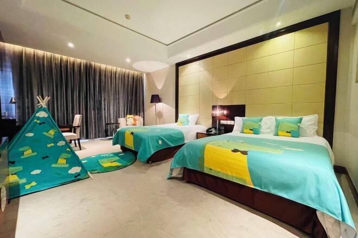A hotel room with two beds, a large window, a curtain, a lamp, and a small tent-like structure.
