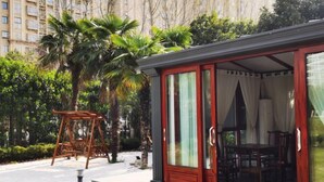 A covered outdoor seating area with a table and chairs, surrounded by lush greenery and palm trees. - Jiangyan Hotel (Taizhou)