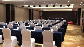 A conference room with rows of tables and chairs, a stage, and a carpeted floor.