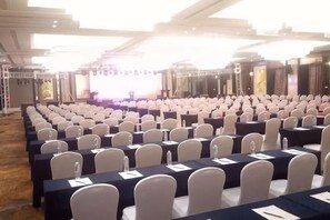 A conference room with rows of tables and chairs, a stage with a screen, and a large window. - Jiangyan Hotel (Taizhou)
