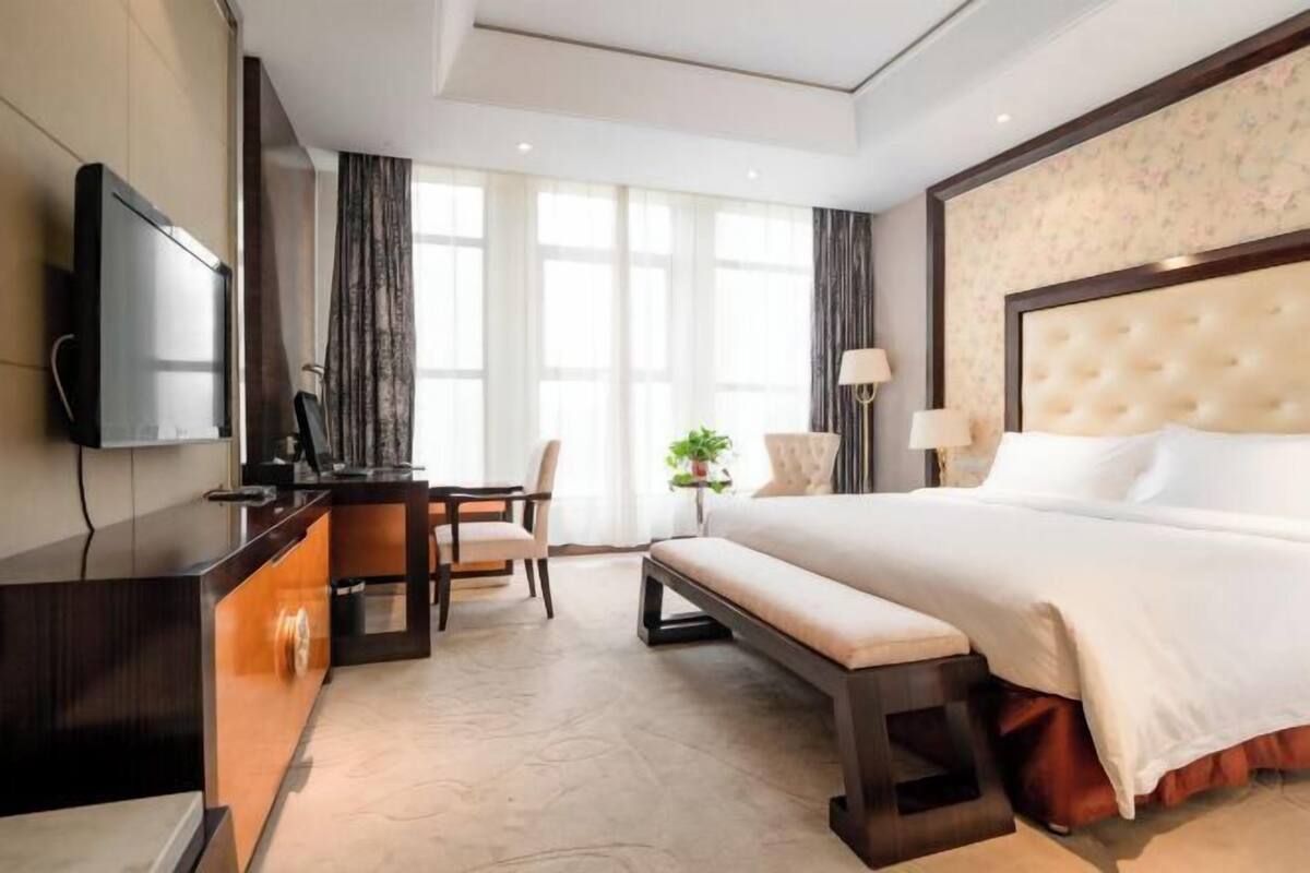 A hotel room with a large bed, a desk with a chair, a television, and a window with curtains.