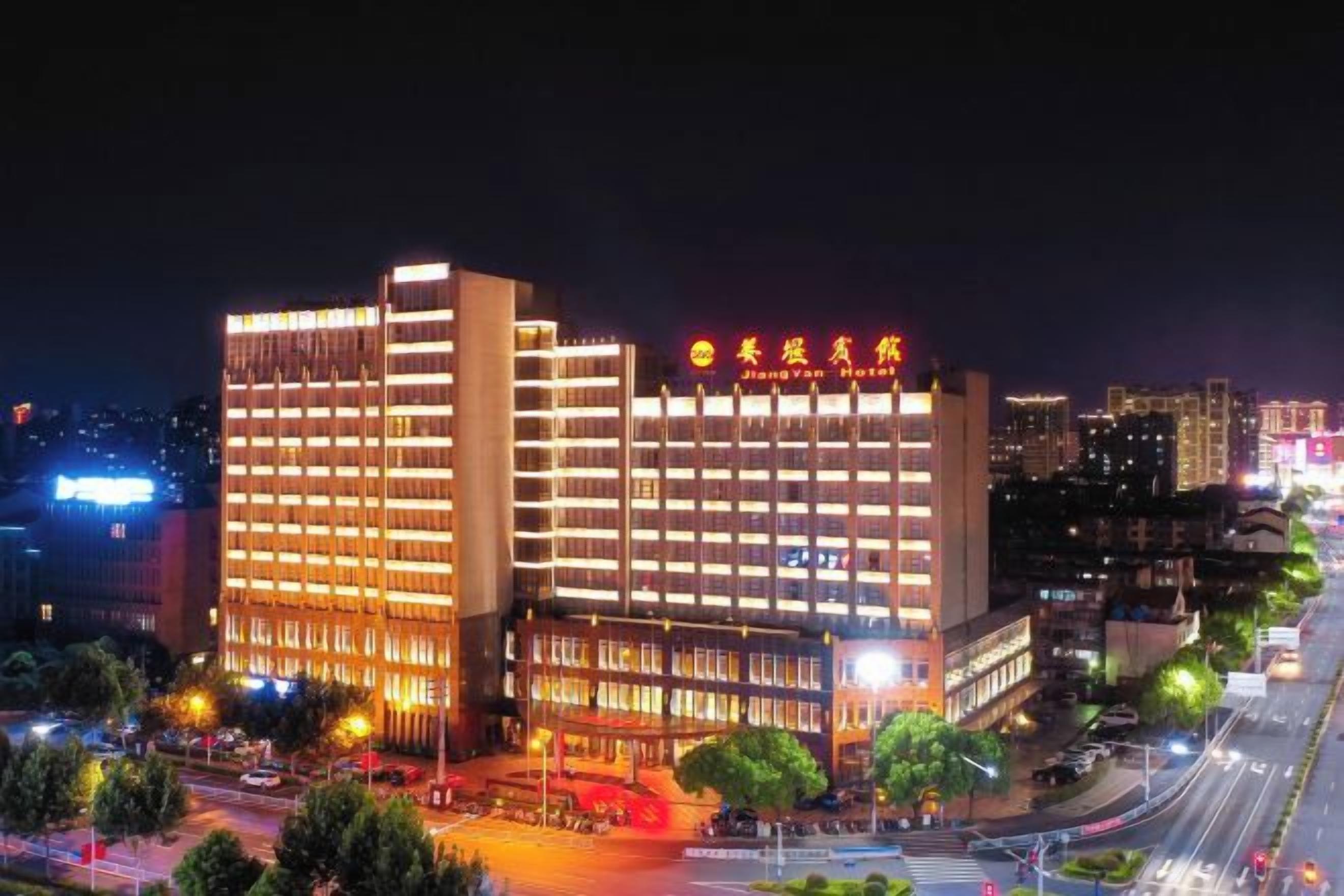 A multi-story hotel with illuminated signage, a well-lit facade, and a busy street in the foreground.