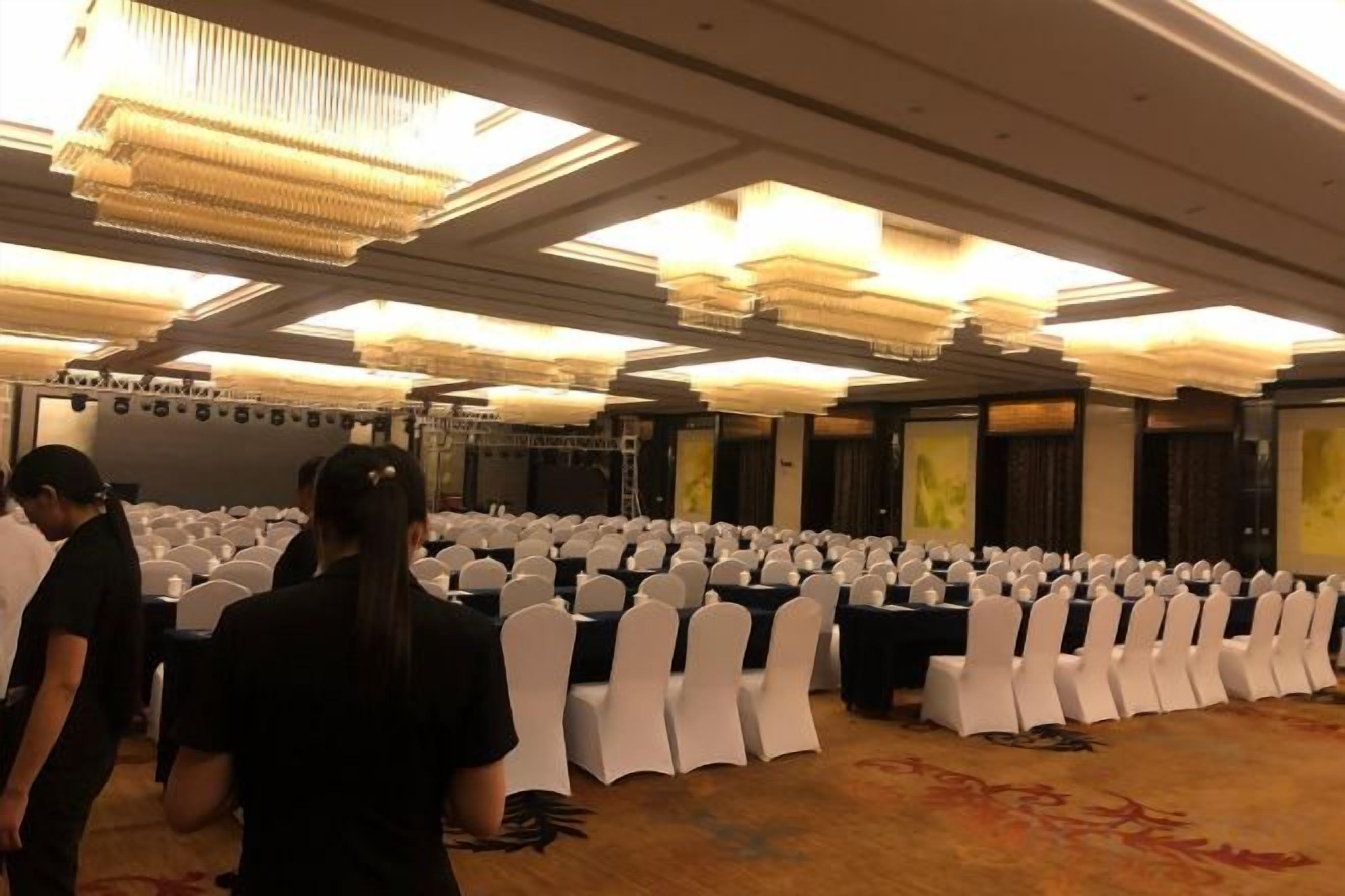 A banquet hall with rows of tables and chairs, a stage, and a chandelier.