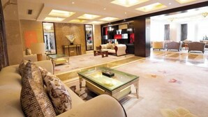 A spacious living room with a large sofa, a glass coffee table, and a fireplace. There is a dining area with a table and chairs visible in the background. - Jiangyan Hotel (Taizhou)