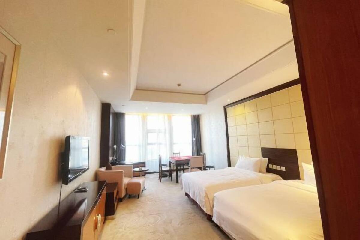 A hotel room with two beds, a desk, a chair, a TV, and a large window.