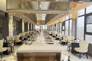 A long dining area with tables and chairs, a central island, and large windows offering a city view. - Jiangyan Hotel (Taizhou)