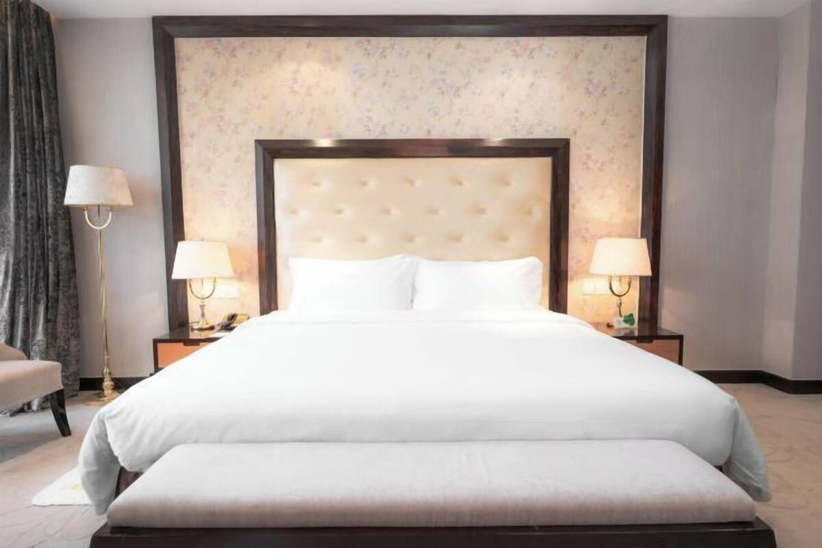 A hotel room with a large bed, two bedside lamps, a chair, and a floral wallpaper.