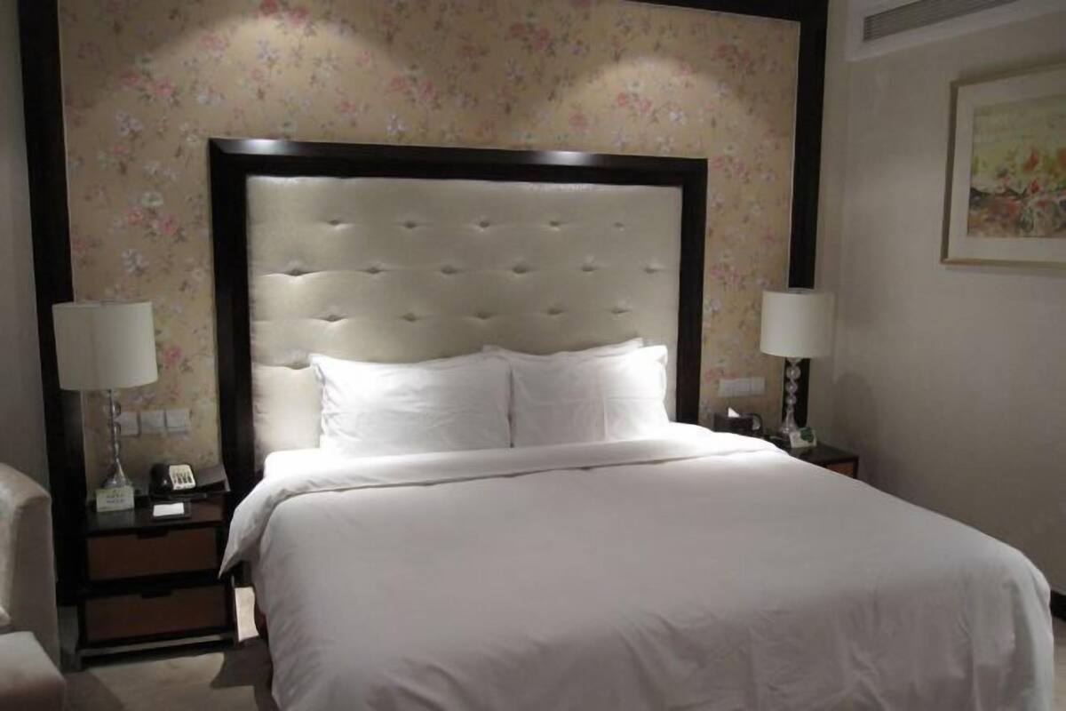 A hotel room with a large bed, two bedside tables with lamps, and floral wallpaper.