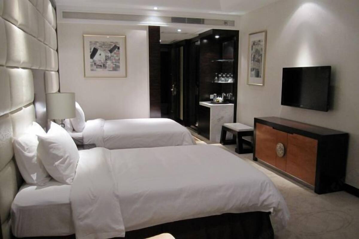 A hotel room with two beds, a TV, a small table, and a cabinet.