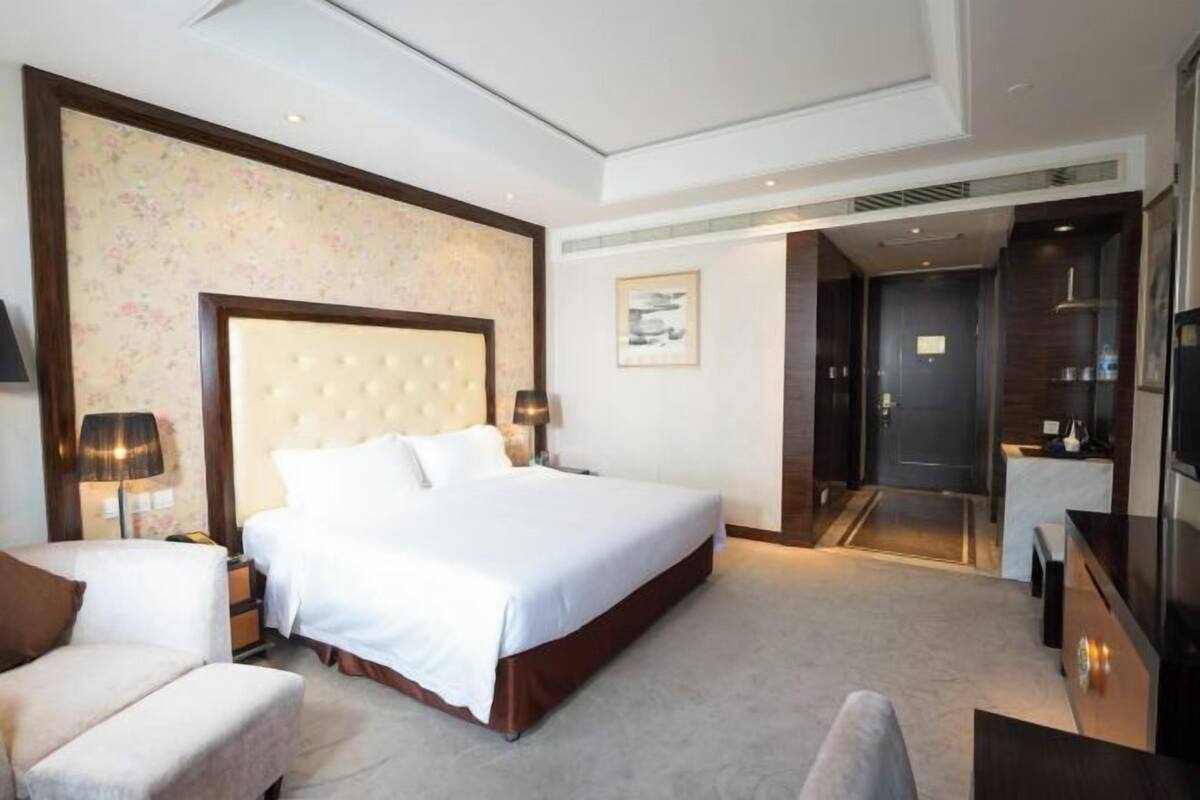 A modern hotel room with a large bed, a seating area, a TV, and a bathroom visible through an open door.