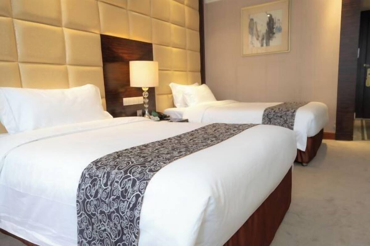 A hotel room with two beds, a large padded headboard, a bedside lamp, and a framed picture on the wall.